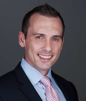 smiling man wearing black suite light blue shirt and polka dot pink tie